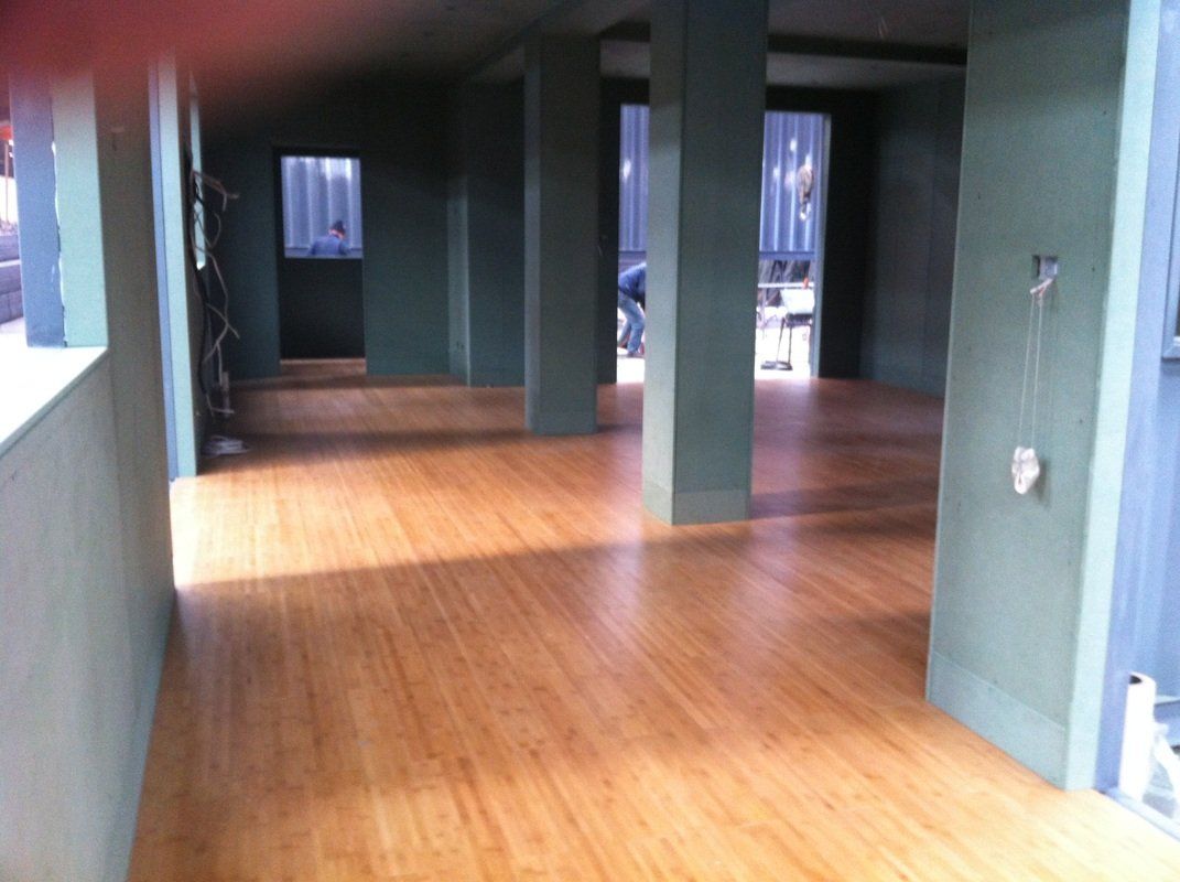 Empty room with bamboo flooring, green columns, and natural light.
