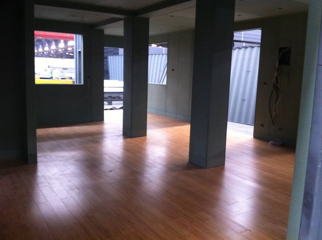 Interior view of a building with hardwood floors, support pillars, and windows looking outside.