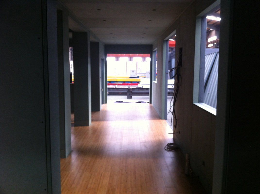 Long hallway with wood floor, doorways, and a view of a street scene at the end.