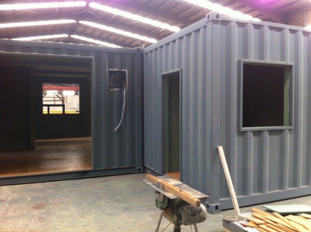 Gray shipping containers assembled into a building, with openings for doors and windows.
