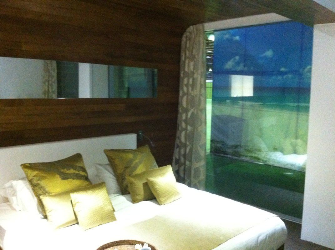 Bedroom with white bed, gold pillows, wooden wall, large window with view of green field.