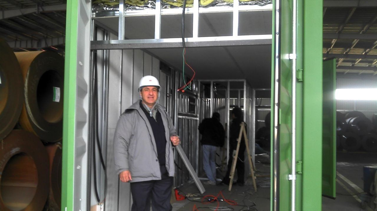 Man in hard hat stands in doorway of a metal frame room under construction.