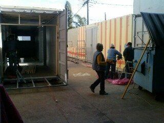 People working near modified shipping containers; one open, another with a ladder.