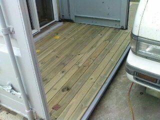 Wooden deck outside a building; a white car is parked nearby.