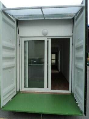 Shipping container converted to a building with sliding door, open doors, and green flooring.