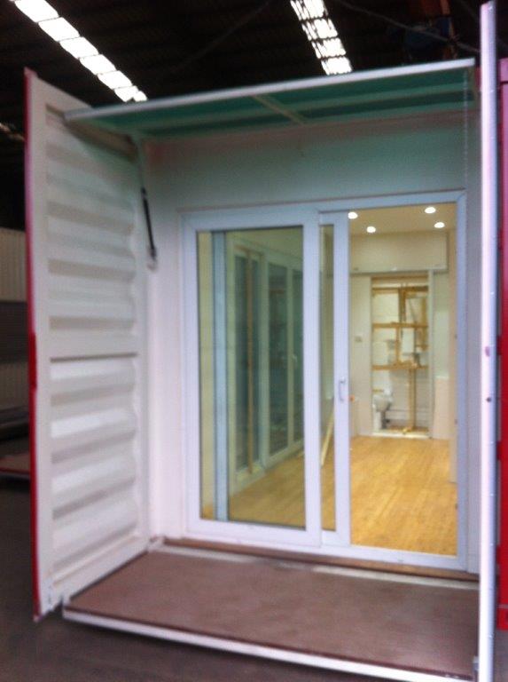 Shipping container converted into a structure with sliding glass door and an awning.