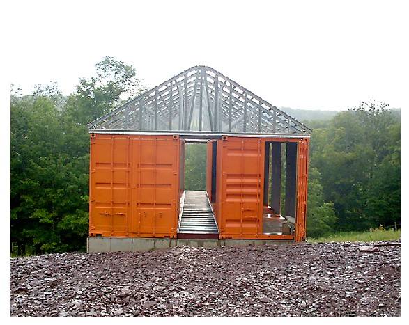 Orange shipping container structure with open doors, under construction, outdoors.