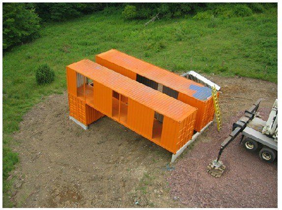 Two orange shipping containers form a modern structure, possibly a house. Crane on right.