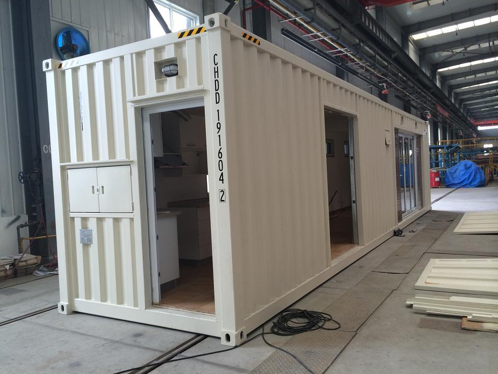 Cream-colored shipping container modified into a building, featuring an open doorway, a cabinet, and two other openings.