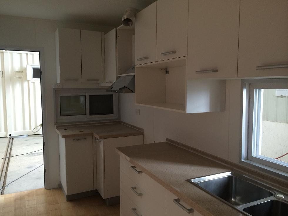 White kitchen cabinets in a room with a window, countertop, sink, and an open doorway.