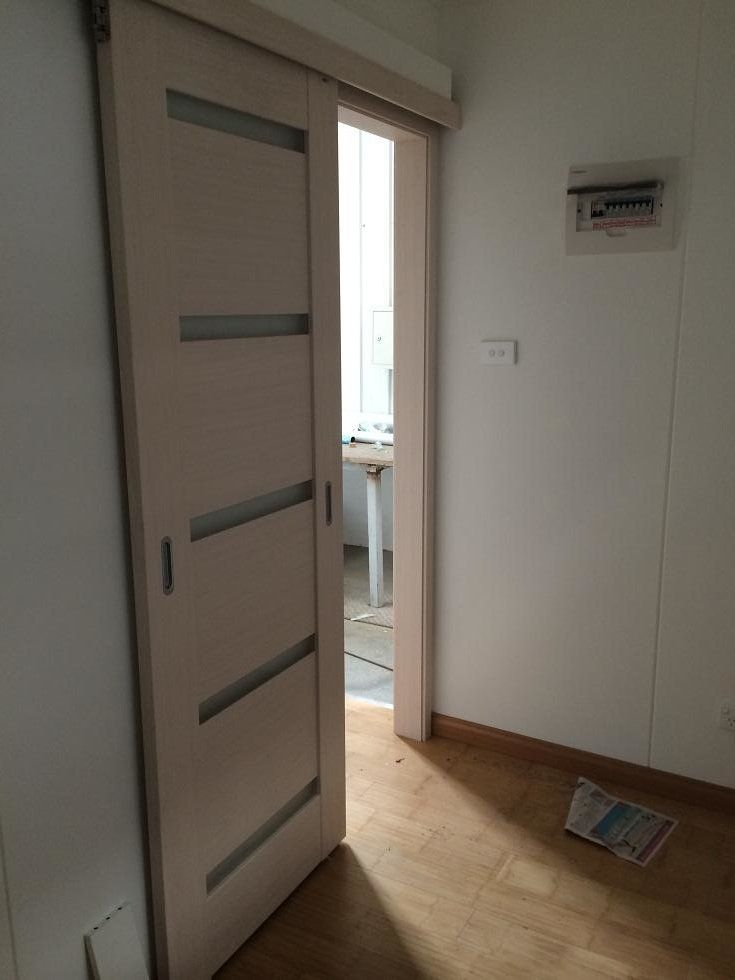 Sliding interior door, partially open. Light wood, frosted glass panels. White walls, wood floor, small room.