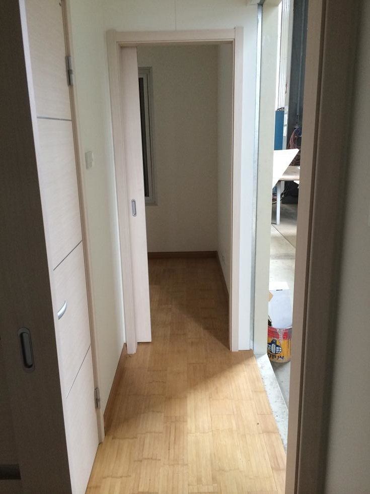 Hallway with wood-look flooring, light doors on the left, and a doorway ahead leading to a room with a window.