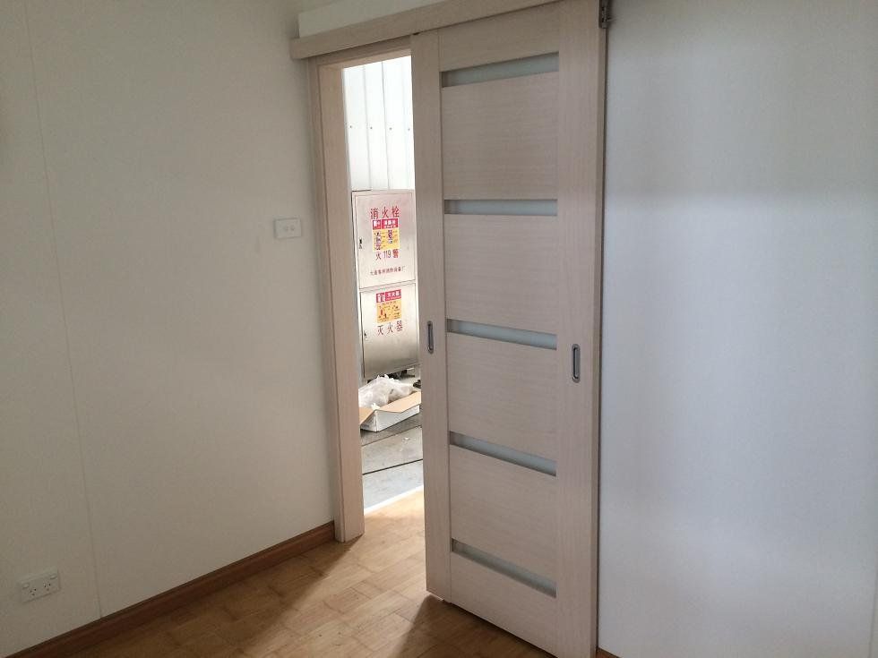 Sliding interior door, partially open. Light wood with frosted glass panels, between rooms with white walls and wood floor.