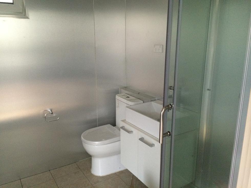 Bathroom with a toilet, sink, and shower enclosed in a frosted glass door. Walls are silver panels.