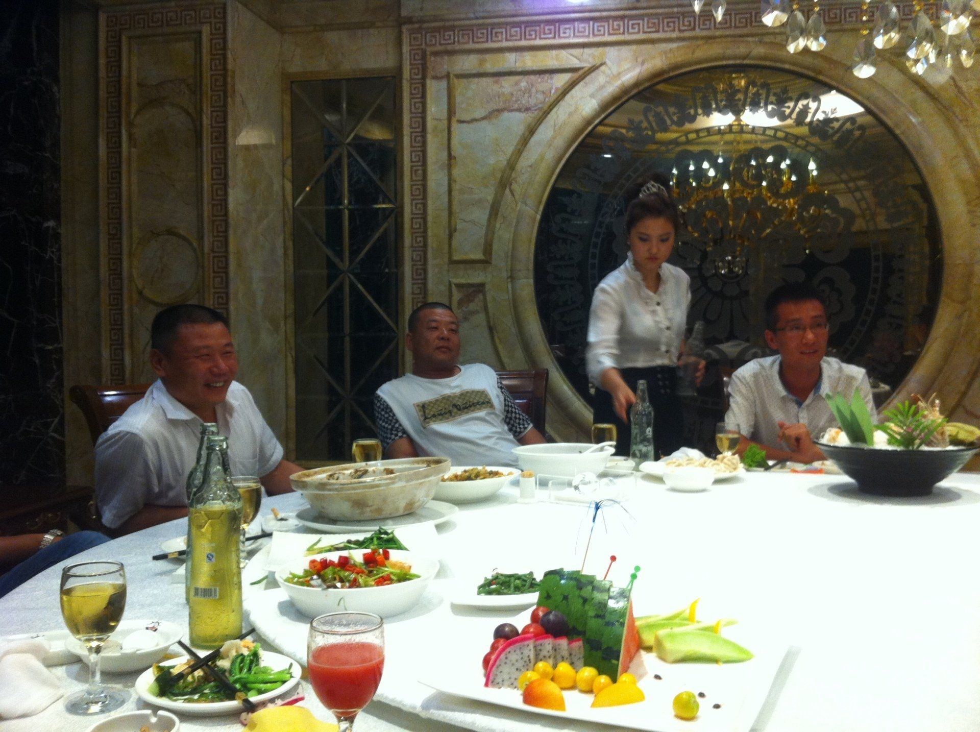 Four people seated at a round table, a server standing nearby; ornate dining room.