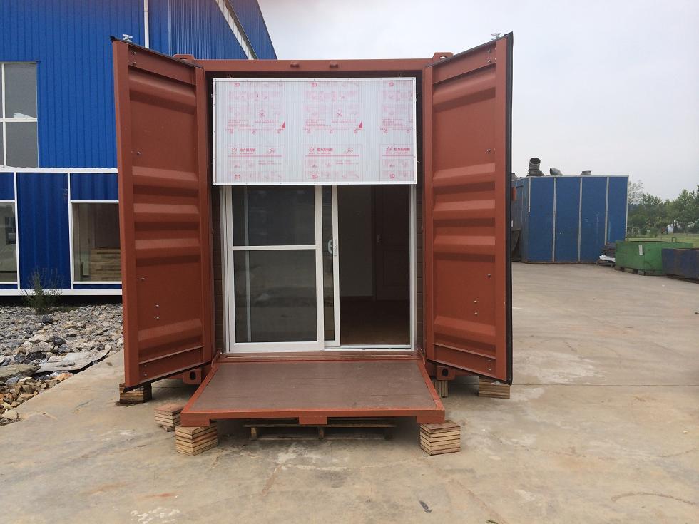 Modified shipping container with open doors, a sliding glass door, and a ramp. Brown exterior, concrete ground.