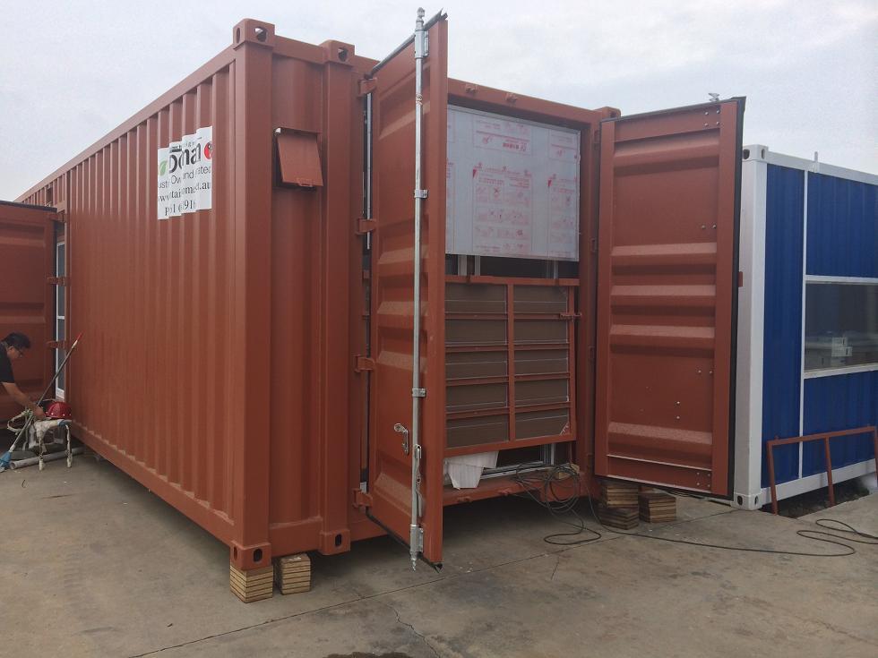 Brown shipping container with open doors, revealing boxes inside; a person works nearby.