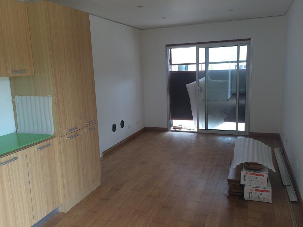 Empty room with wood cabinets, wood floor, sliding glass door leading to balcony.