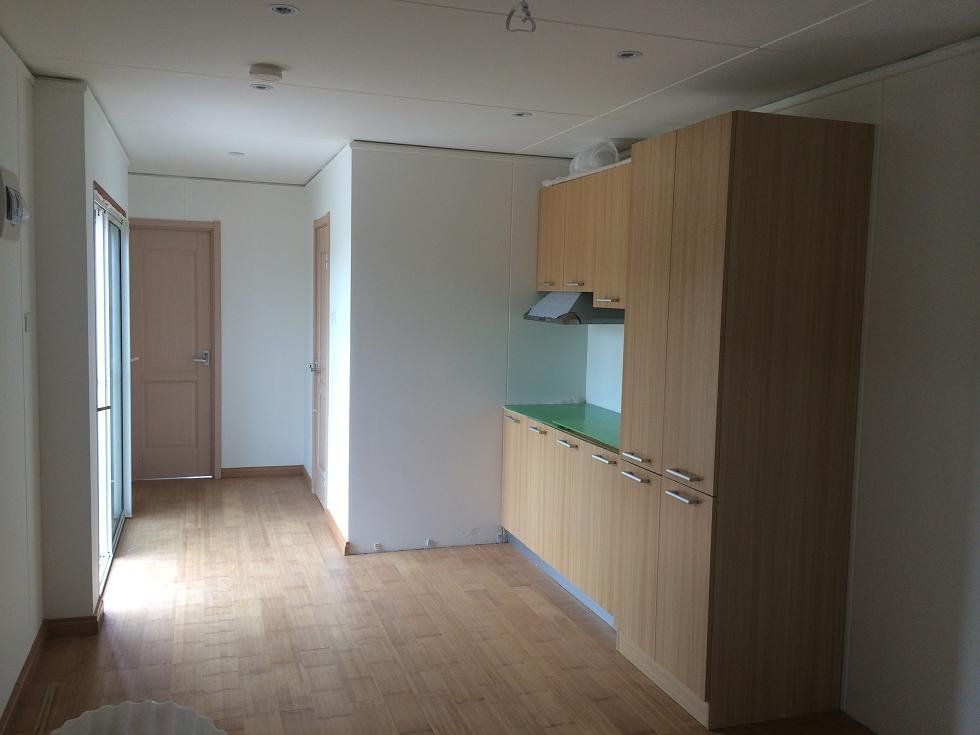 Empty apartment interior with wooden cabinets and flooring, hallway, and a door to a balcony.