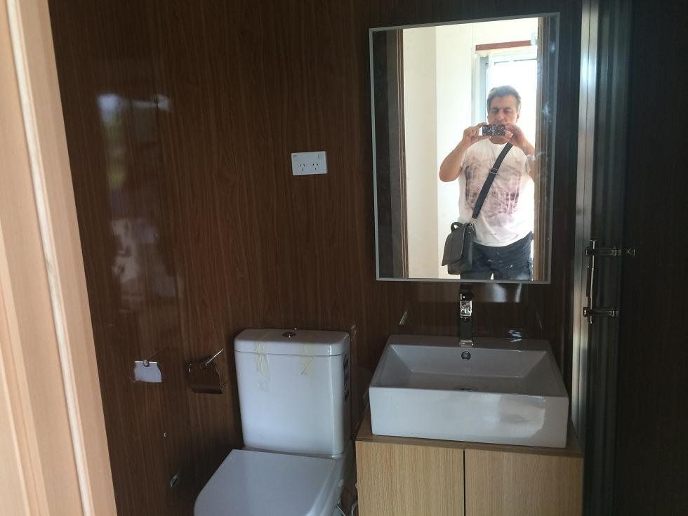 Bathroom with toilet, sink, mirror, and a person taking a photo in the mirror. Brown walls.