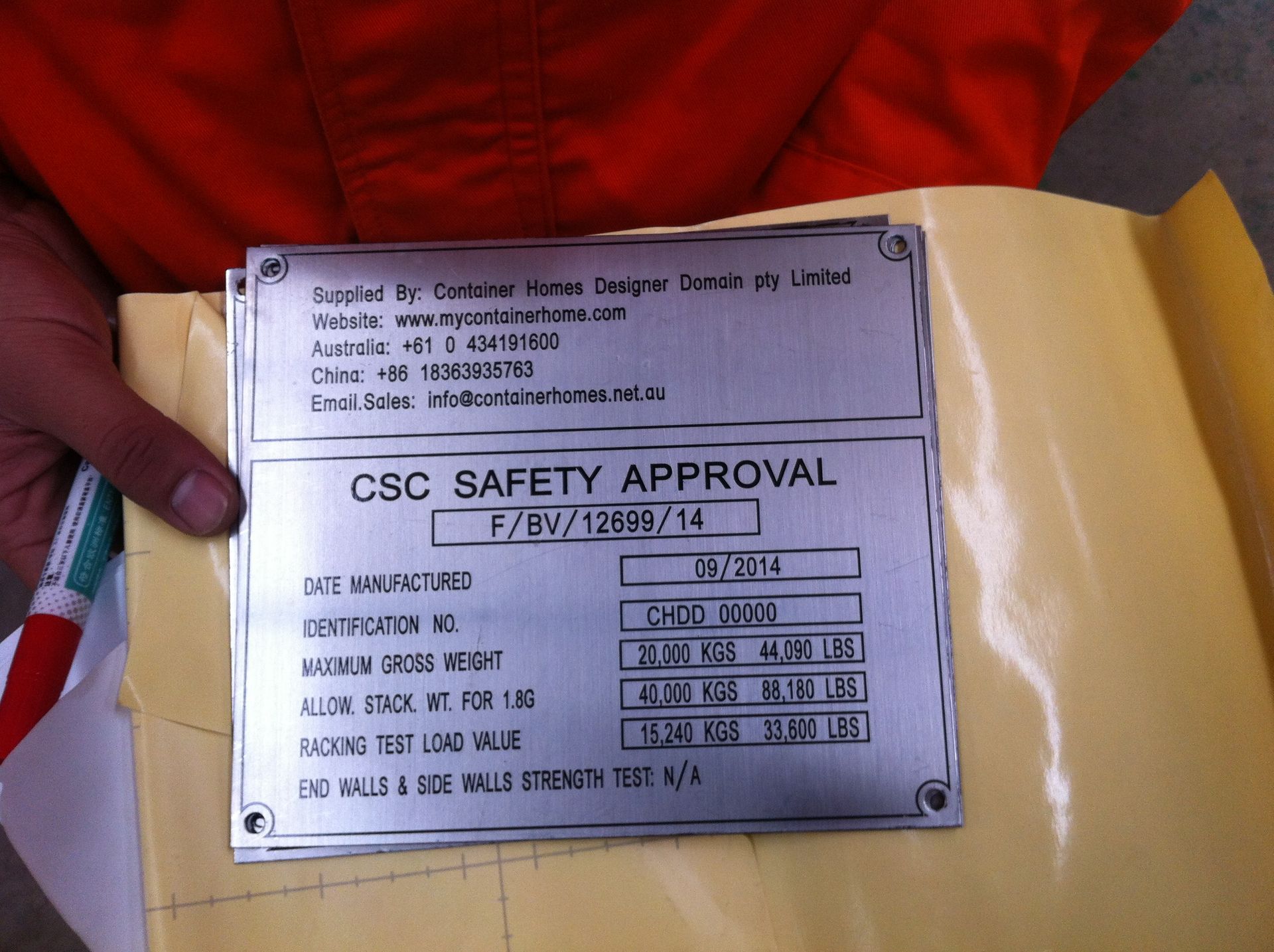 A metal CSC Safety Approval plate with details like date, certification, maximum gross weight, and test load values, held by a person.