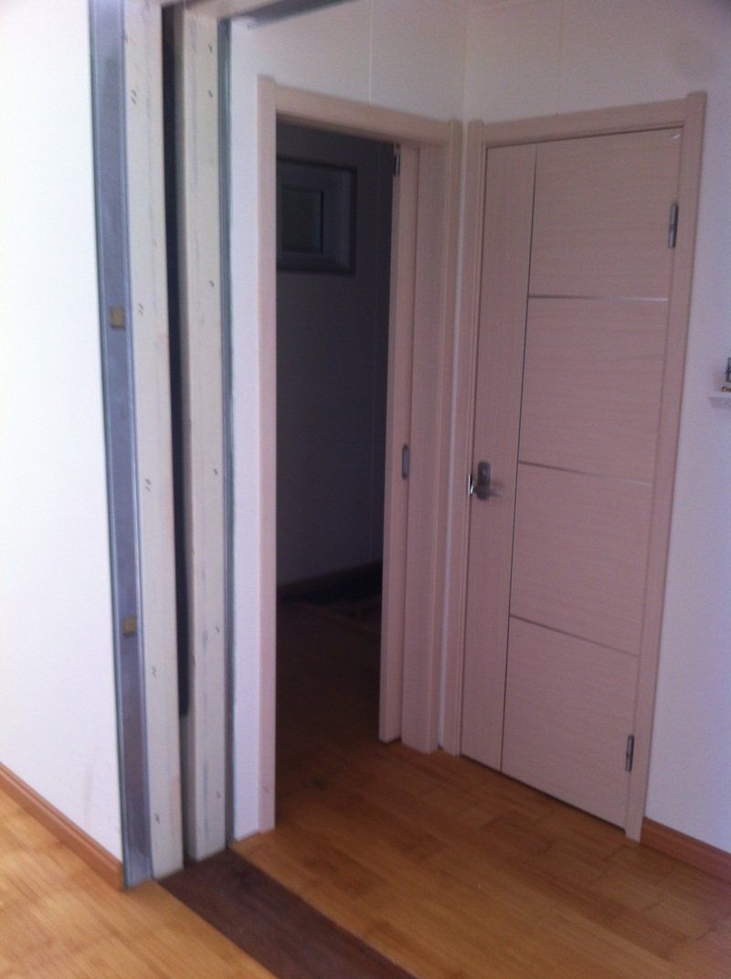 An open door with light beige door and frame. A doorway is to the left, and hardwood floors.