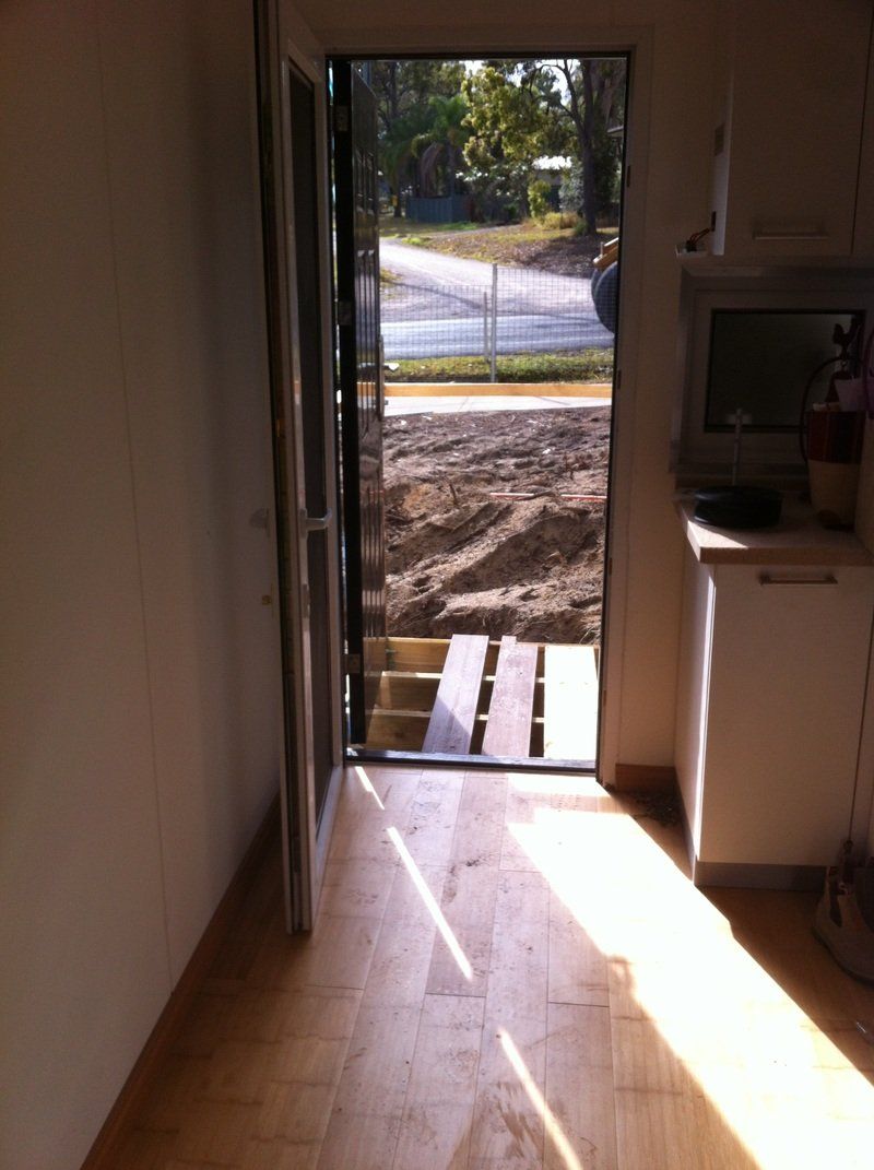 Open doorway with wooden floor leading outside to steps. Sunlight streams in.