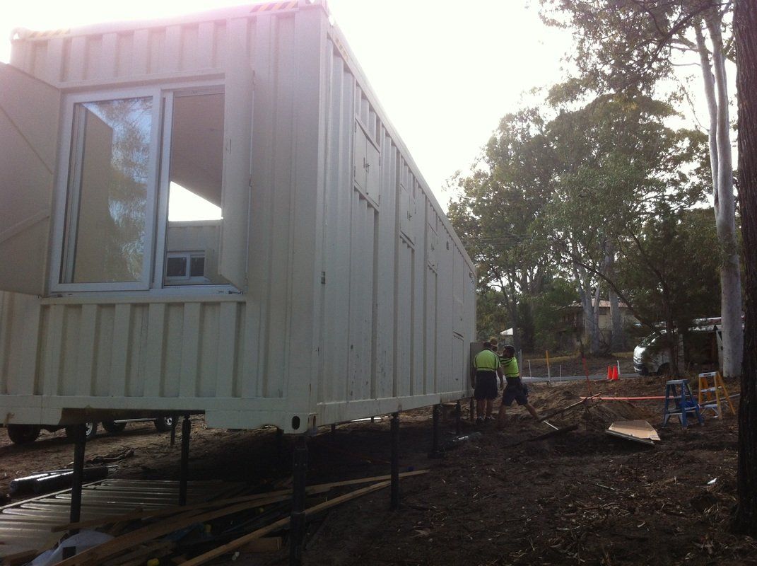 Shipping container being installed; workers near; construction site; exterior.