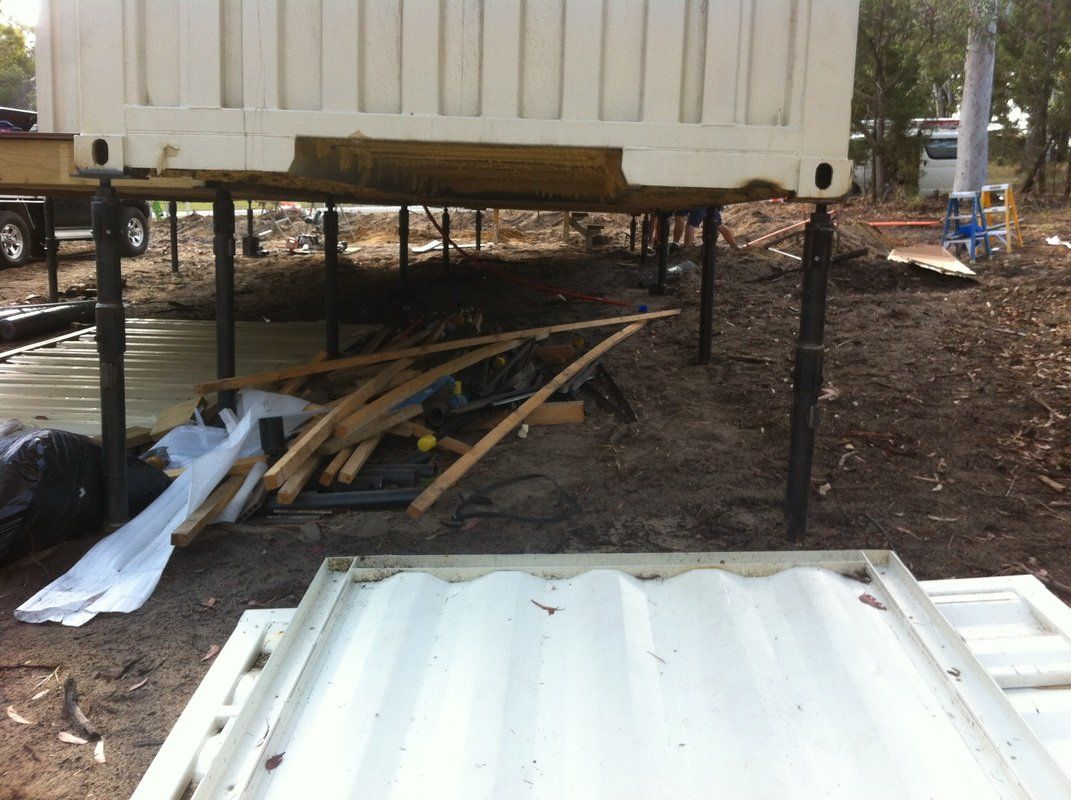Container raised on adjustable supports. Debris and metal sheets on the ground.