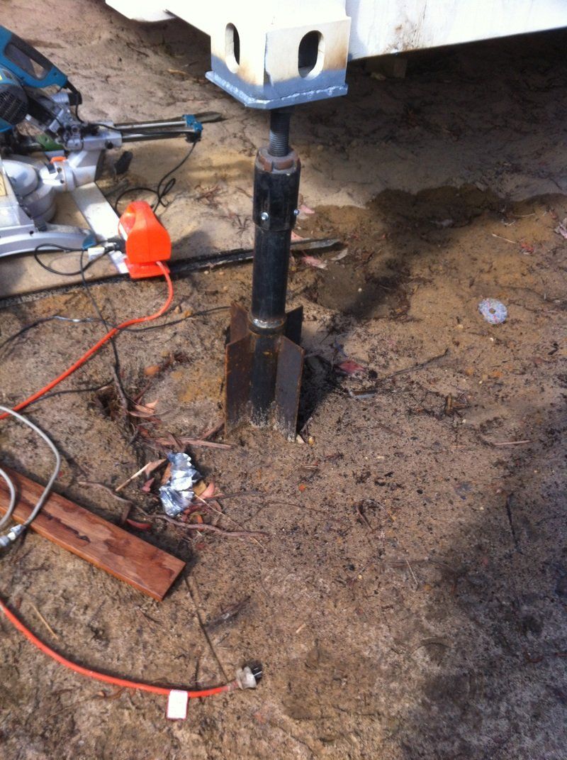 Trailer jack extended on muddy ground, with power tools nearby.