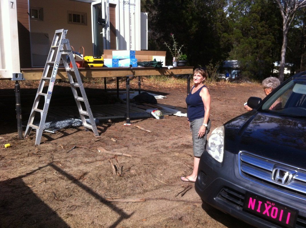 Woman standing by a car near a deck under construction with a ladder, tools, and materials.