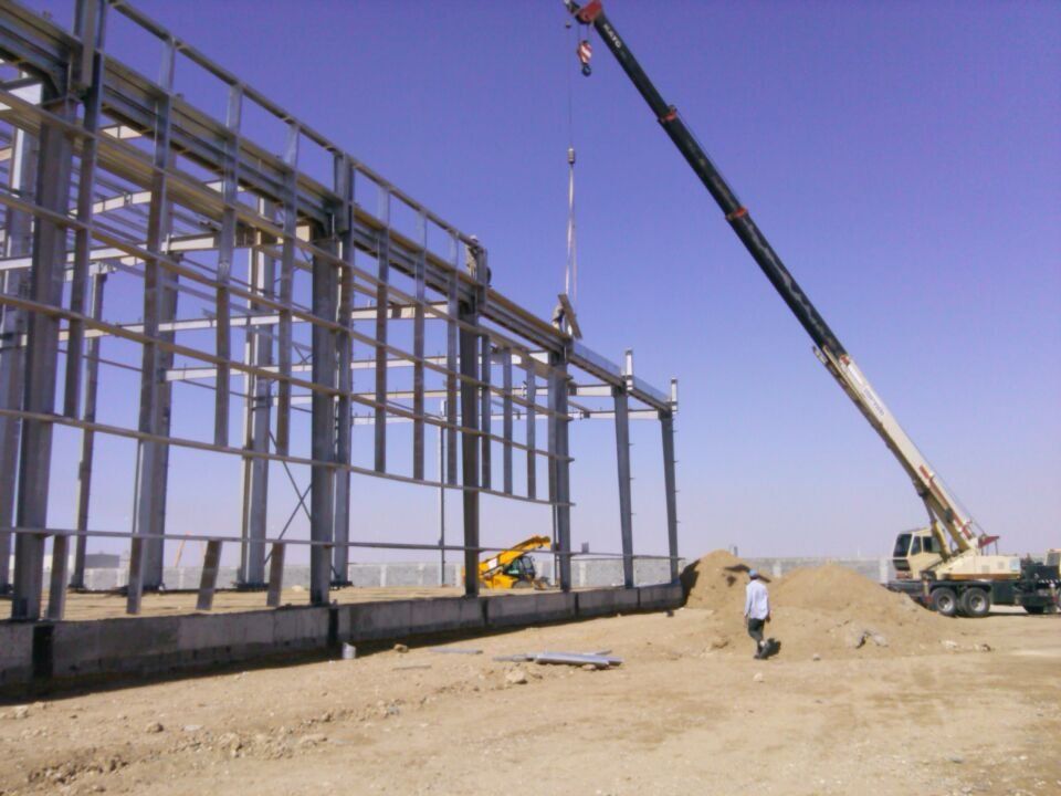 Construction site: crane lifting steel beam for a building frame against a blue sky.