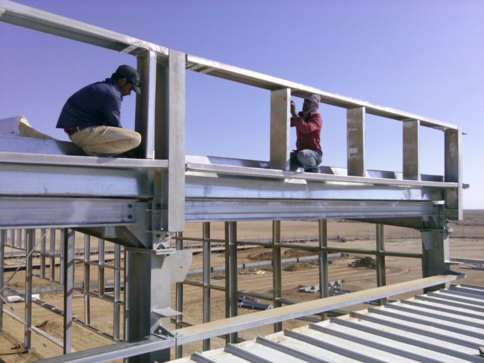 Two workers installing steel framework on a building under construction outdoors.