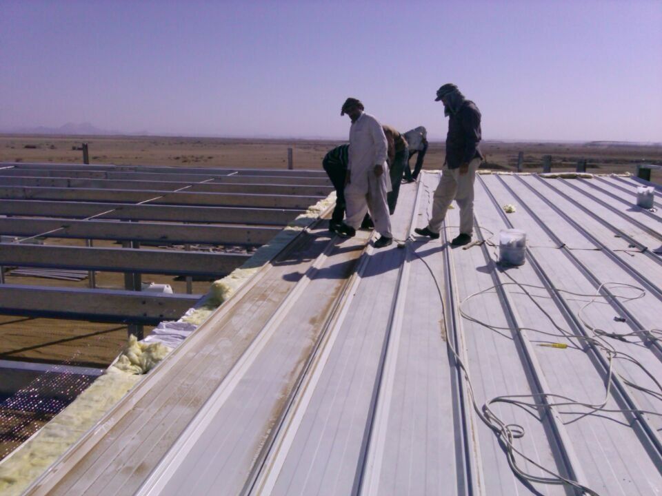 Three workers on a roof installing panels, blue sky in the background.