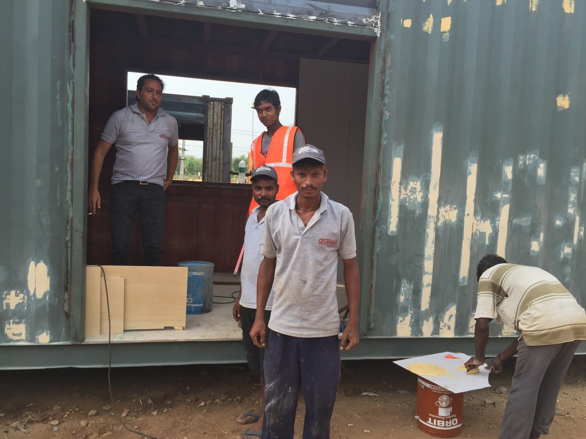 Men standing near a shipping container being worked on. One man is writing on a surface.