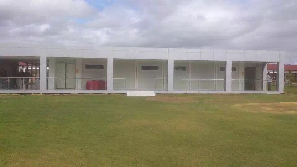 White rectangular building with glass windows on a green lawn, under a cloudy sky.