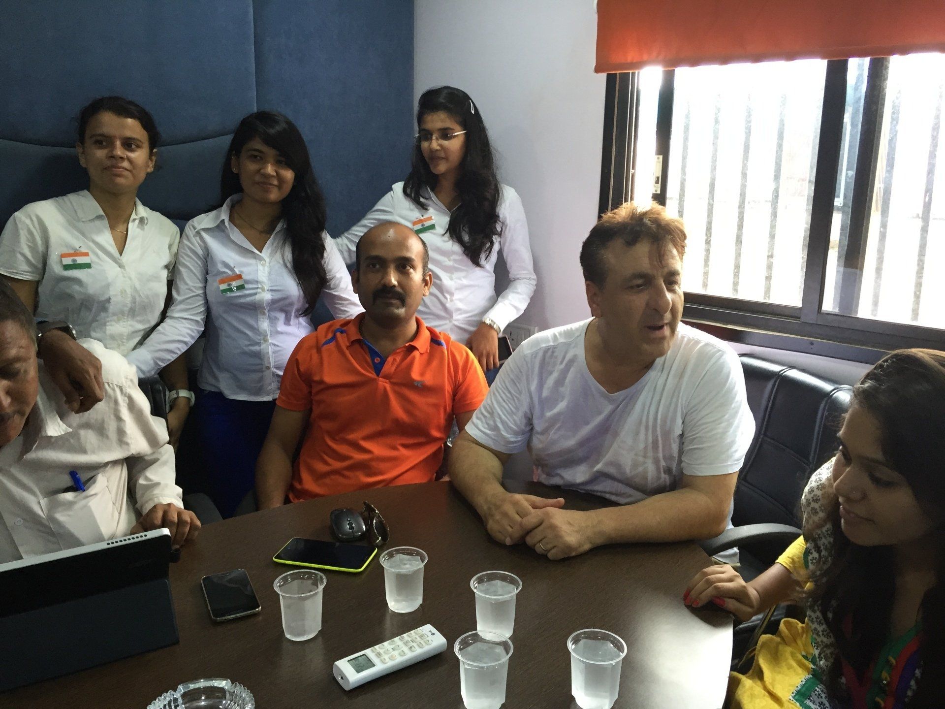 People sitting at a table with glasses of water, some wearing white shirts with a tricolor pin.