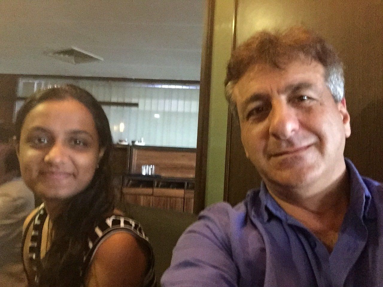Two people smiling at a restaurant. One person is wearing a blue shirt.
