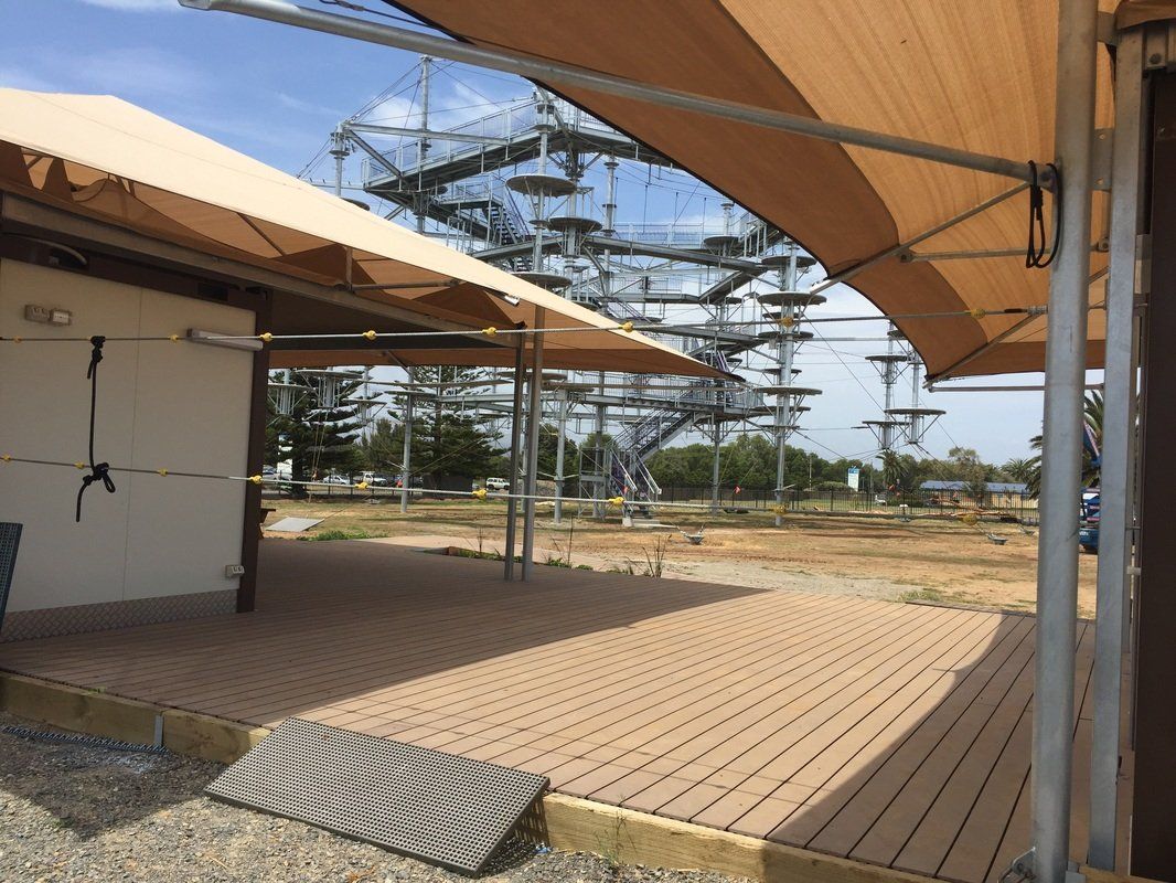 Outdoor deck with shade sails, overlooking a high ropes adventure course.
