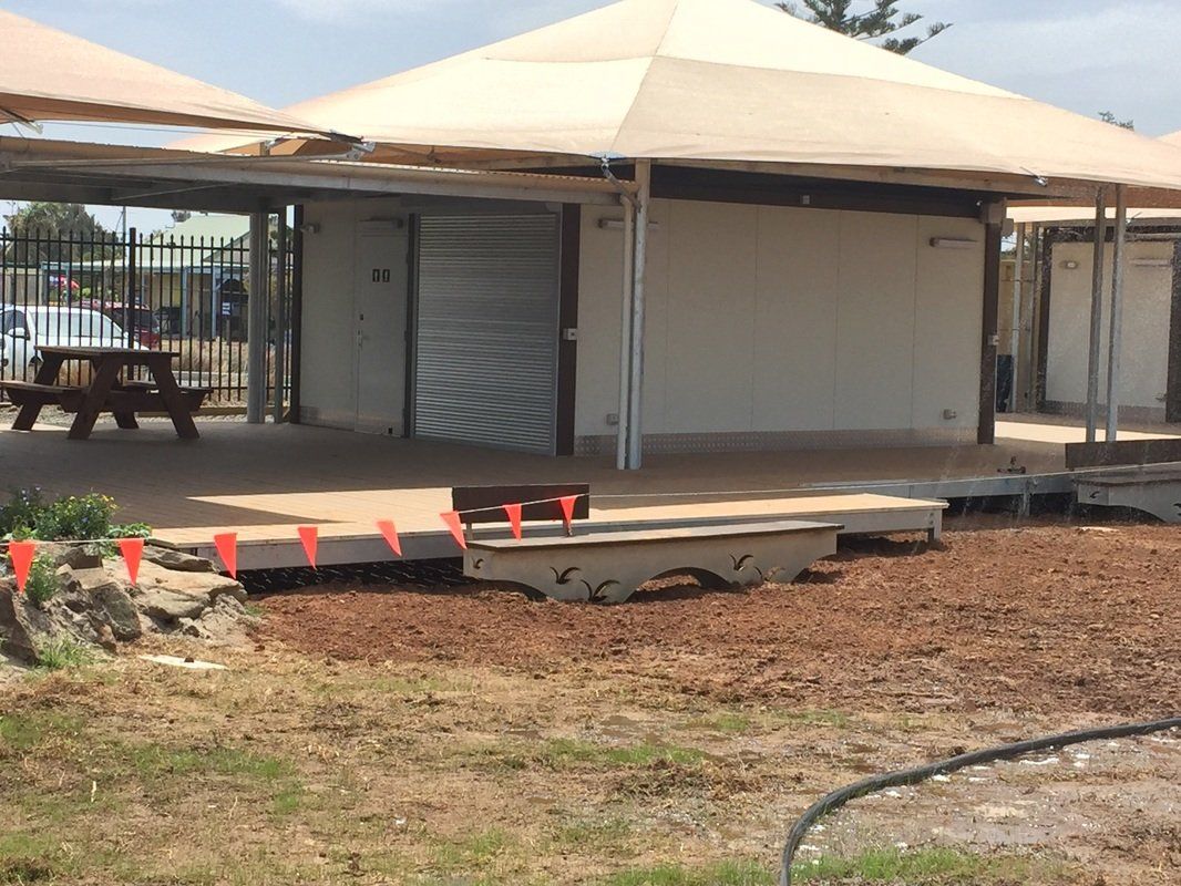 Covered outdoor structure with a bench, picnic table, and landscaping.