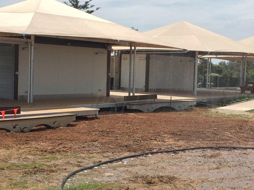 Tan canvas-roofed structures with open sides, on raised platforms, sitting on a patch of dirt and grass.