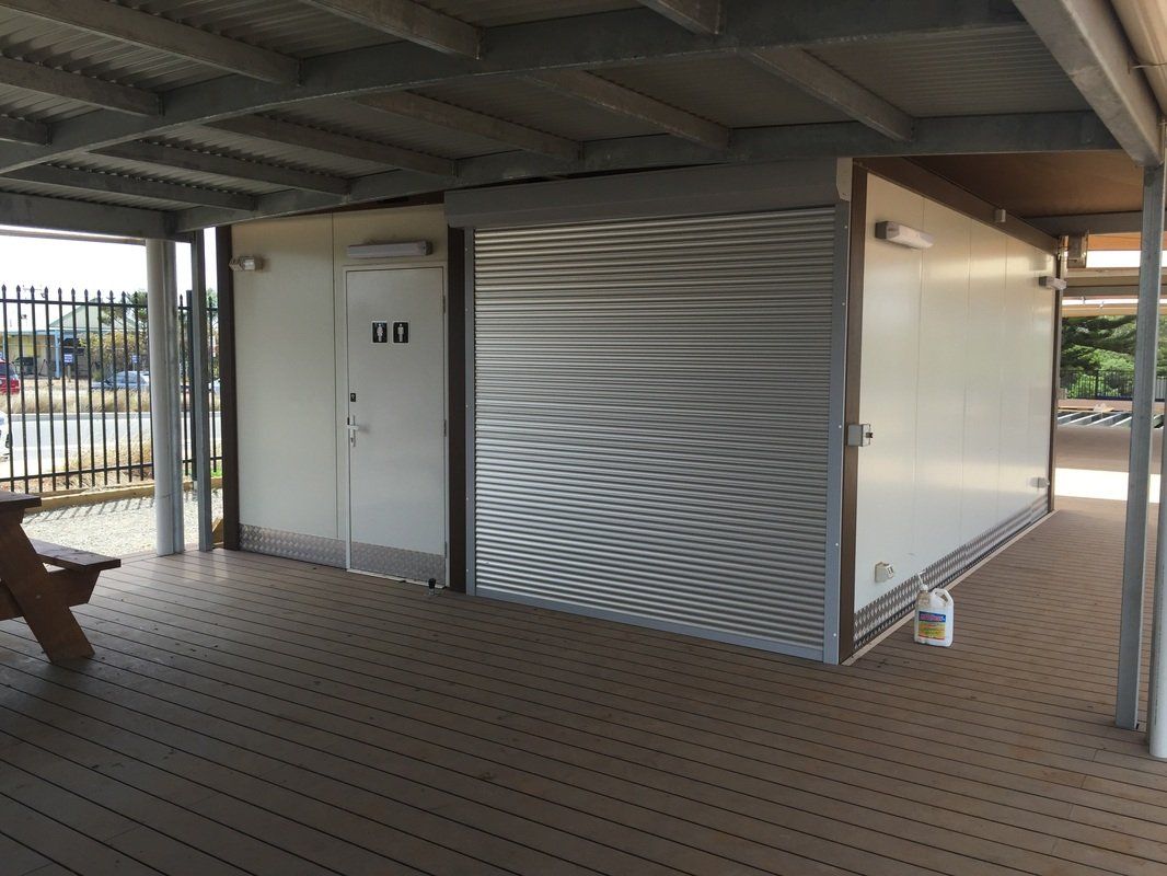 Public restroom building with a metal shutter, under a covered patio.