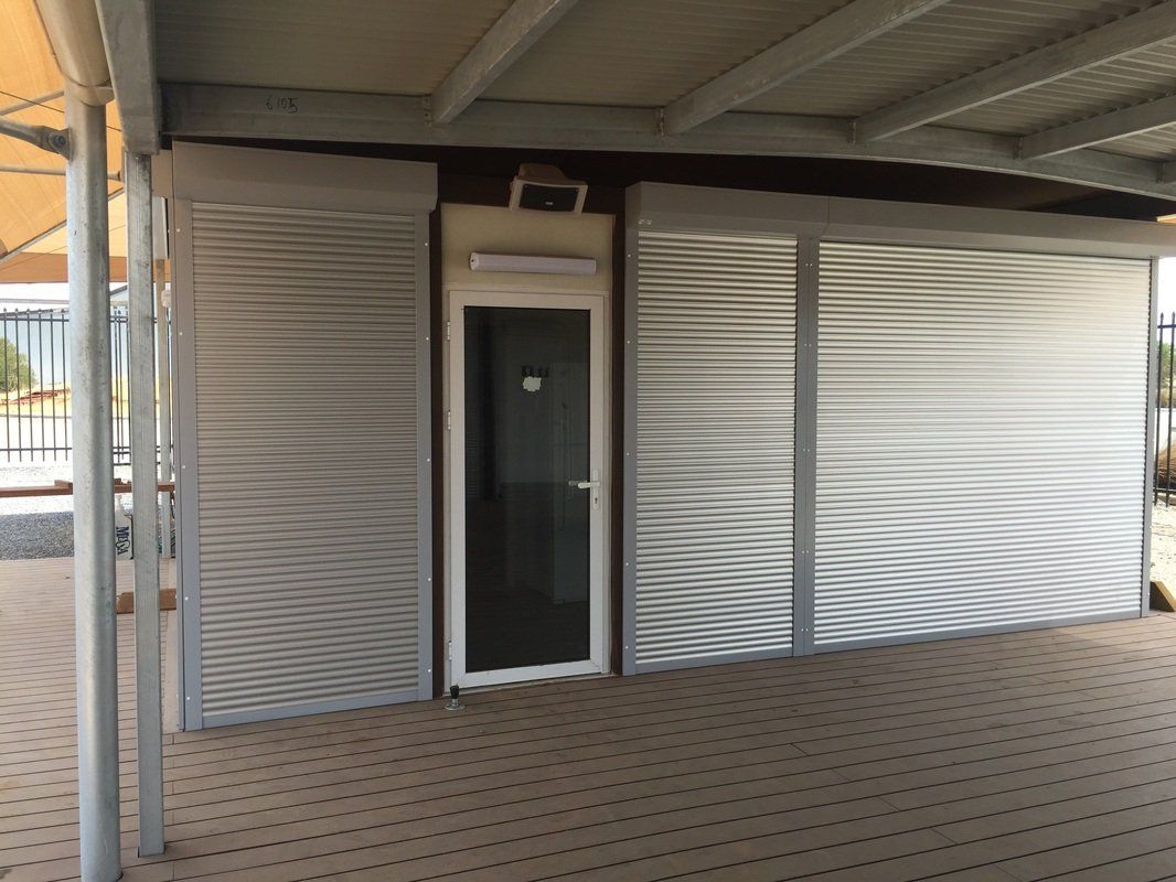 A small building with roll-up metal doors and a glass door under a covered area.