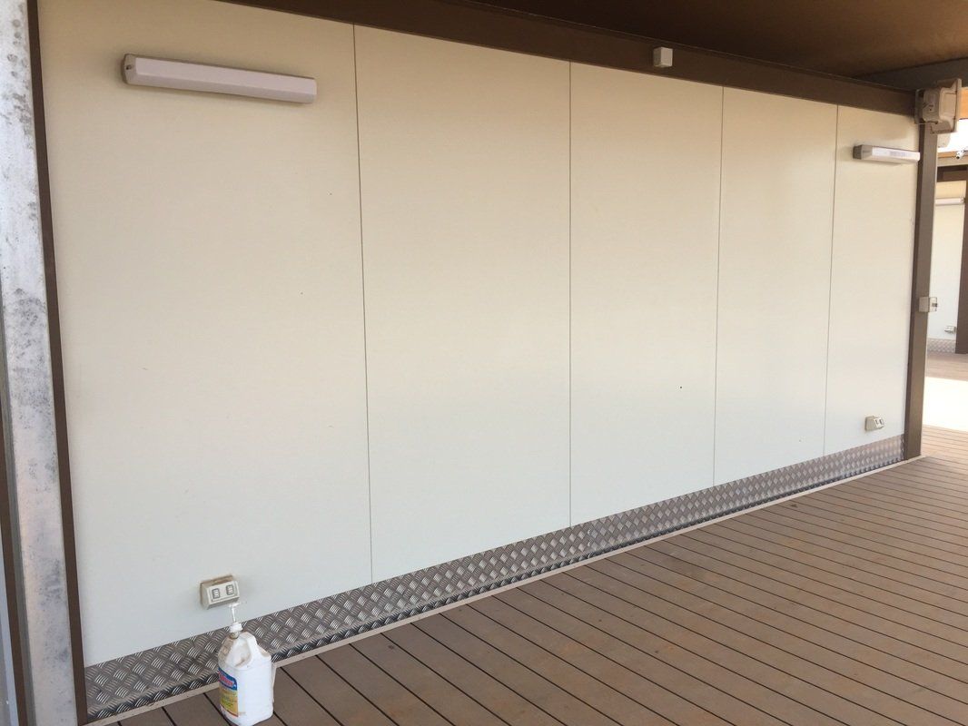 White paneled wall with metal trim, two lights, electrical outlet, and a bottle on a brown deck.