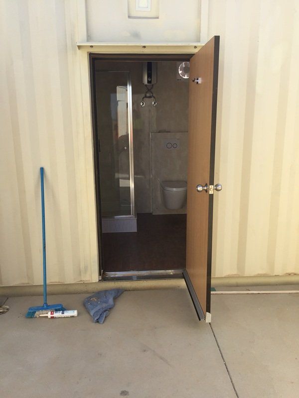 Open door to a bathroom, revealing a shower and toilet. A broom and mop rest nearby.