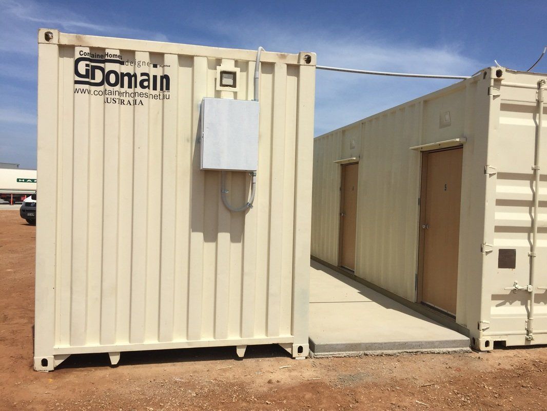 Two beige shipping containers connected by a concrete ramp. One has a white box attached.