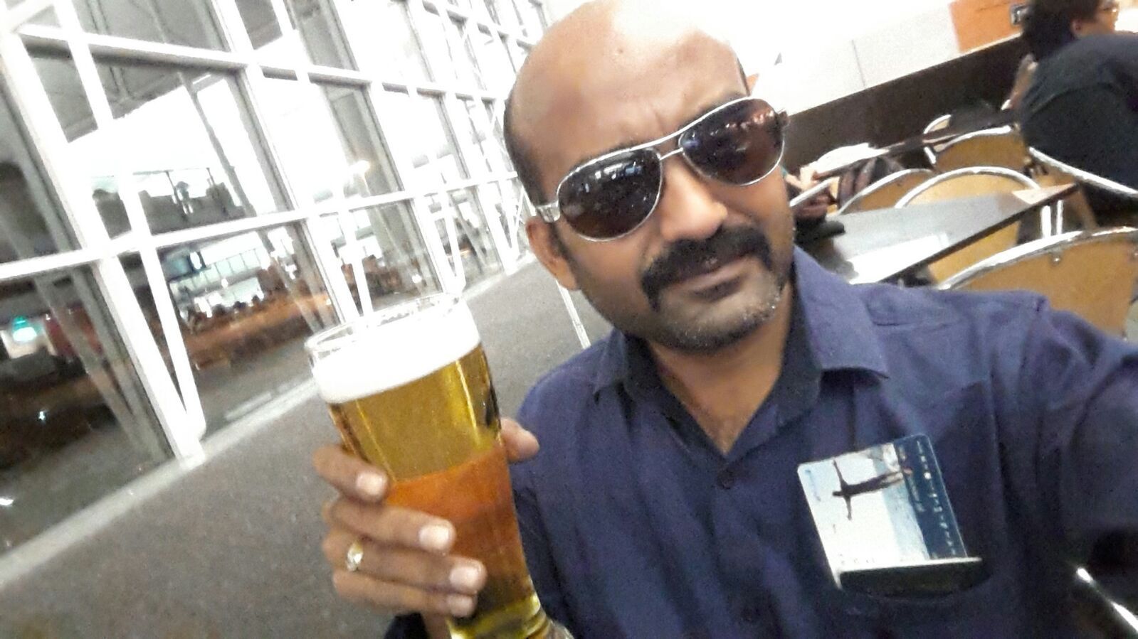 Man with sunglasses holding a beer in a restaurant, looking at the camera.