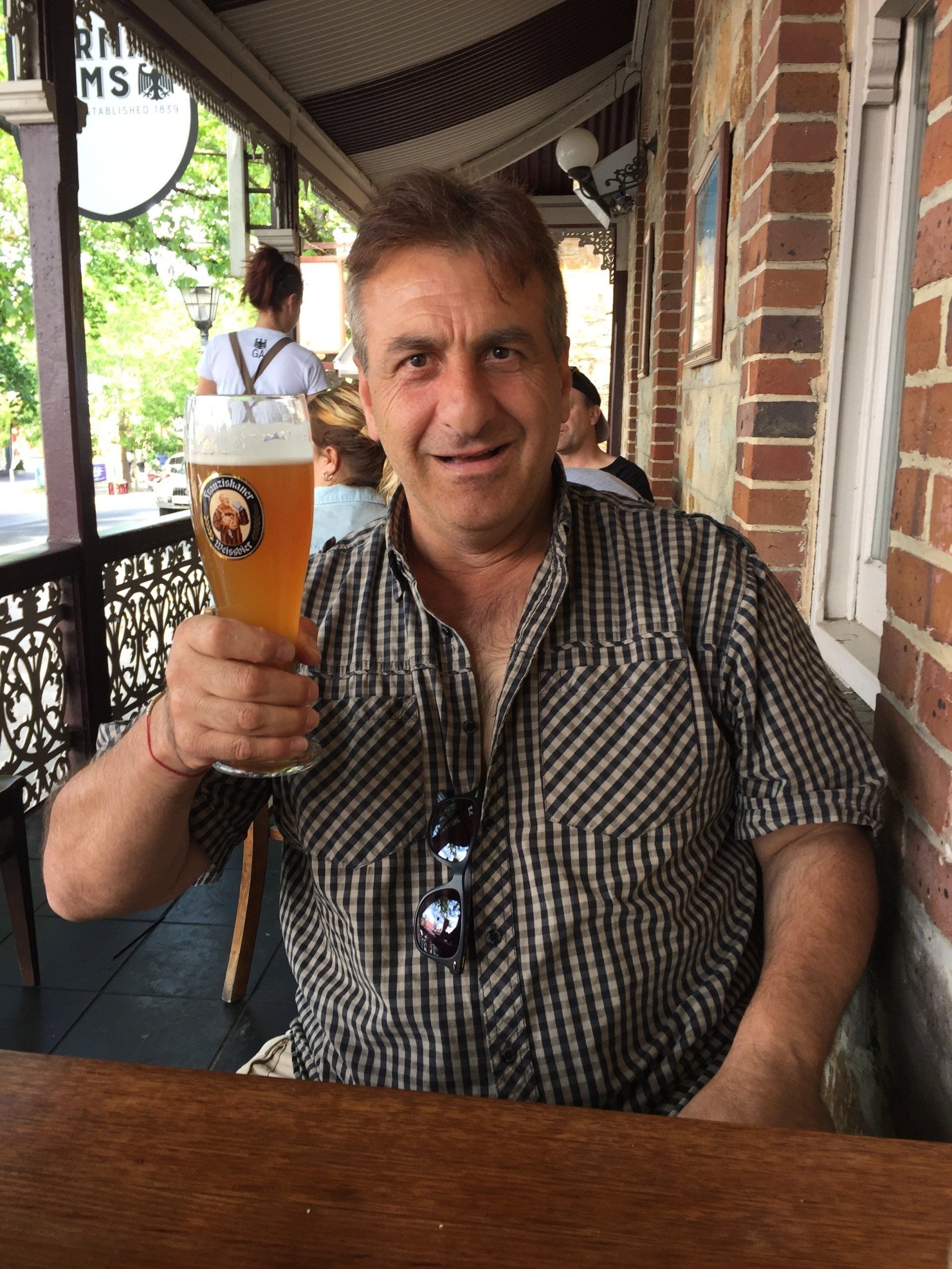 Man raising a beer glass at an outdoor cafe. He is smiling.