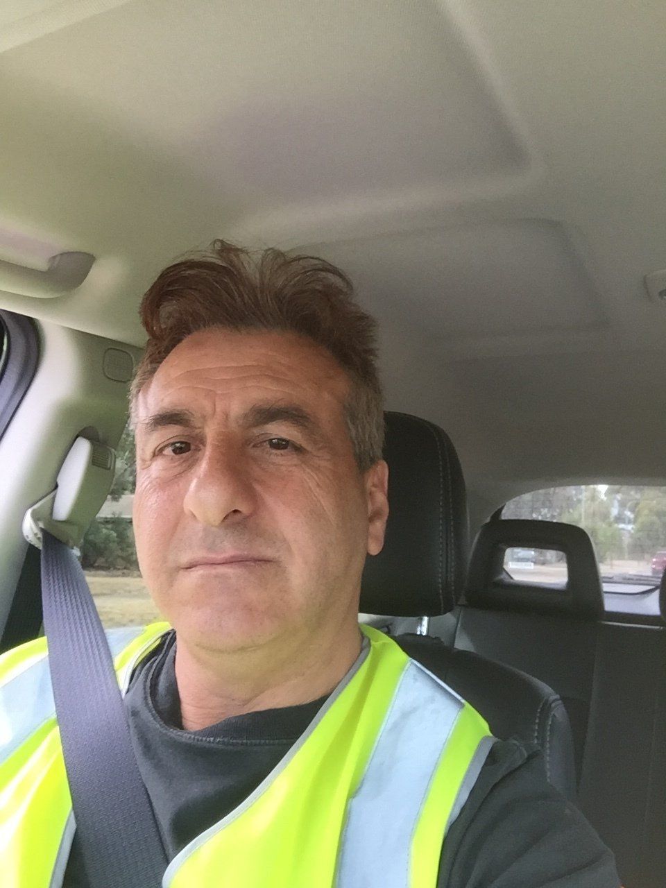 Man wearing a high-visibility vest sits in a car, looking at the camera.