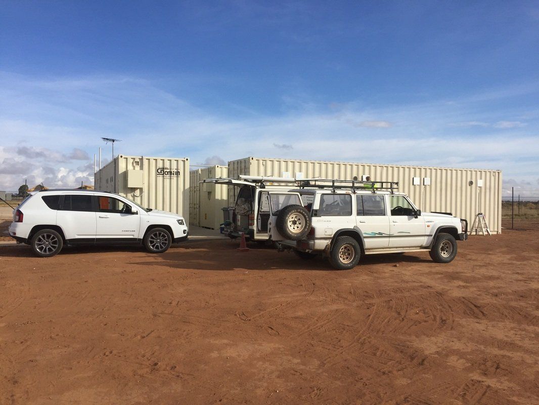 White SUV and Jeep with trailer parked near storage containers in a dirt lot.